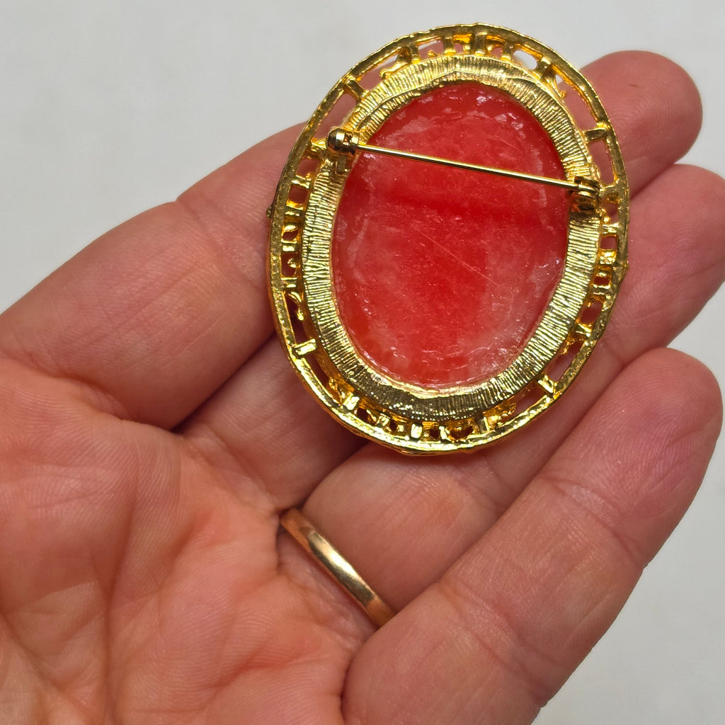 Elegante Vintage-Kamee-Brosche im Goldrahmen – Klassische Frauen-Silhouette auf rötlichem Hintergrund