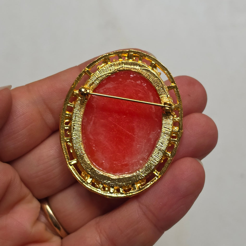 Elegante Vintage-Kamee-Brosche im Goldrahmen – Klassische Frauen-Silhouette auf rötlichem Hintergrund